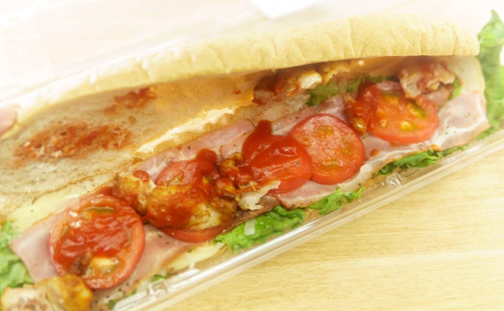 炙り焼きチキンのBLTCモンスターバケットサンドの中に挟まれているトマトやレタス・ハムなどの具材